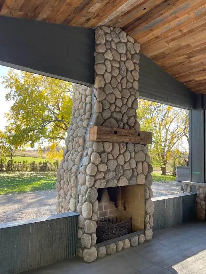 A large stone fireplace is under a wooden roof.