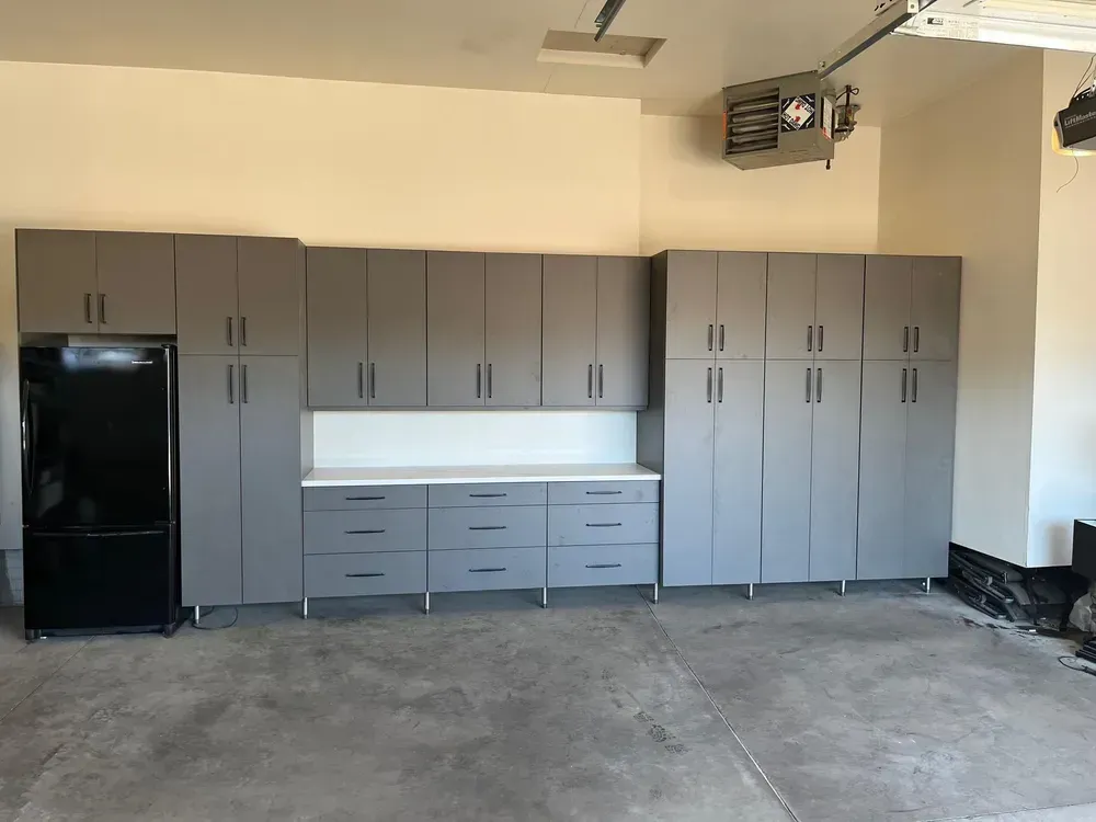 A garage with lots of cabinets and drawers and a refrigerator.
