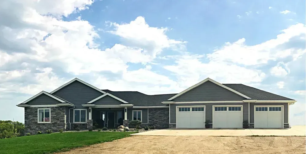 A large house with three garage doors is sitting on top of a dirt field.