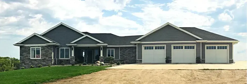 A large house with three garage doors is sitting on top of a dirt field.