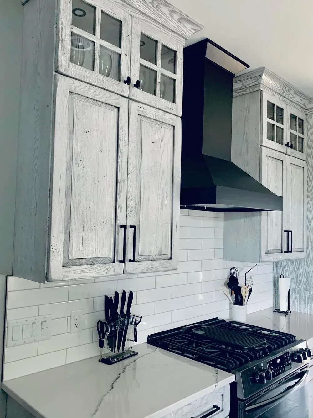 A kitchen with white cabinets , a stove , and a black hood.