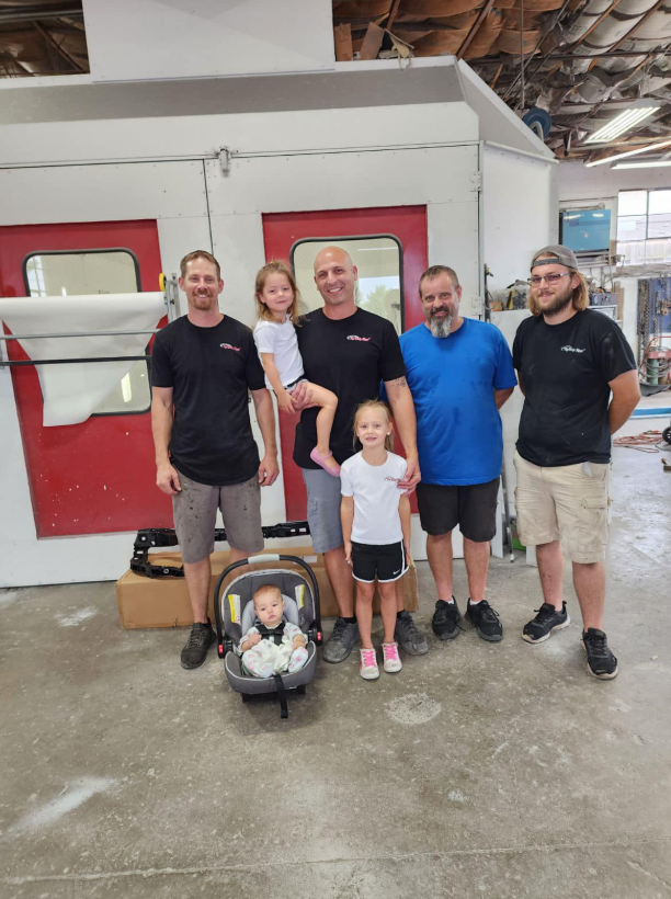 A group of people are posing for a picture in a garage with a baby in a car seat.