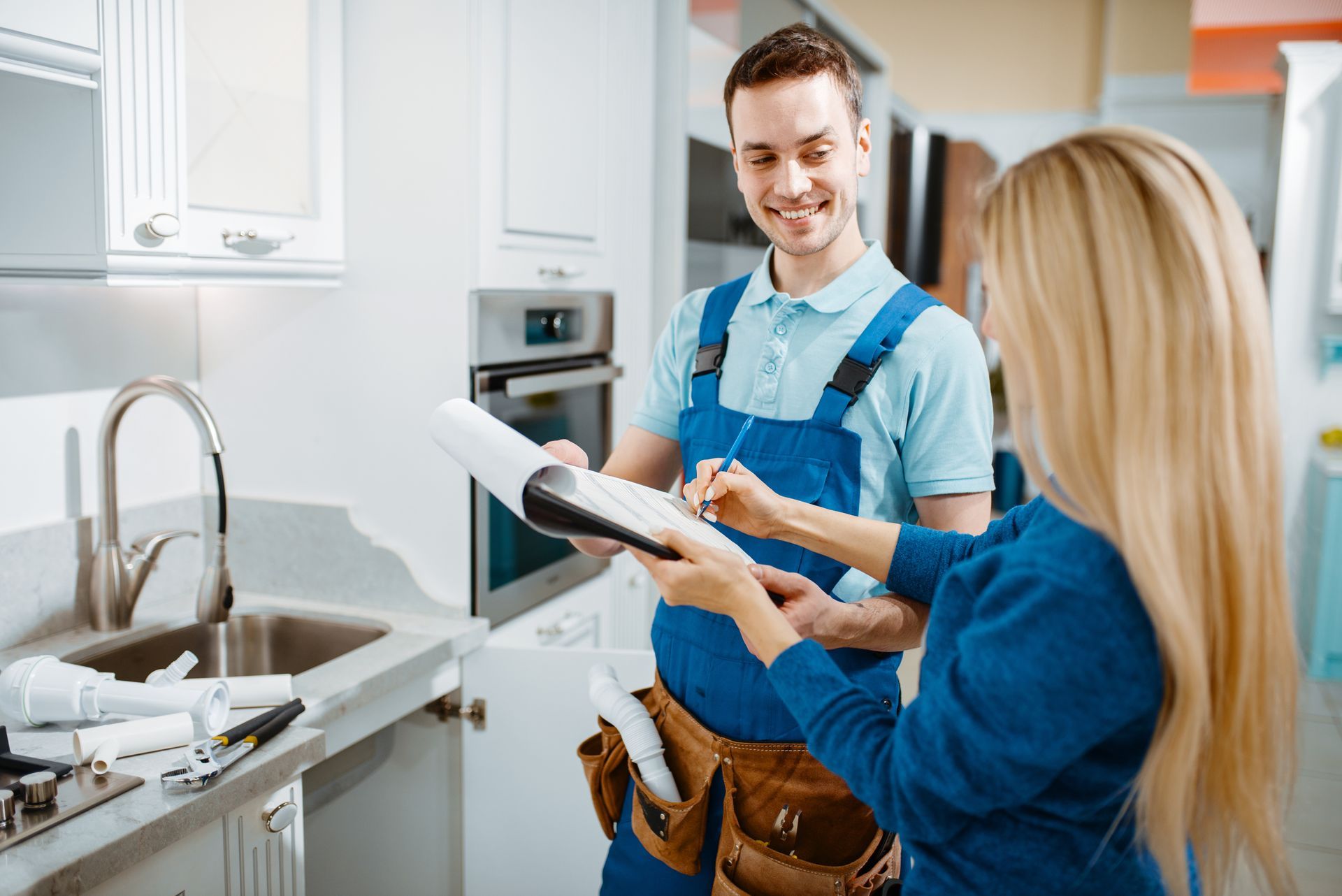 Customer signs paperwork with home service technician beside a kitchen sink.