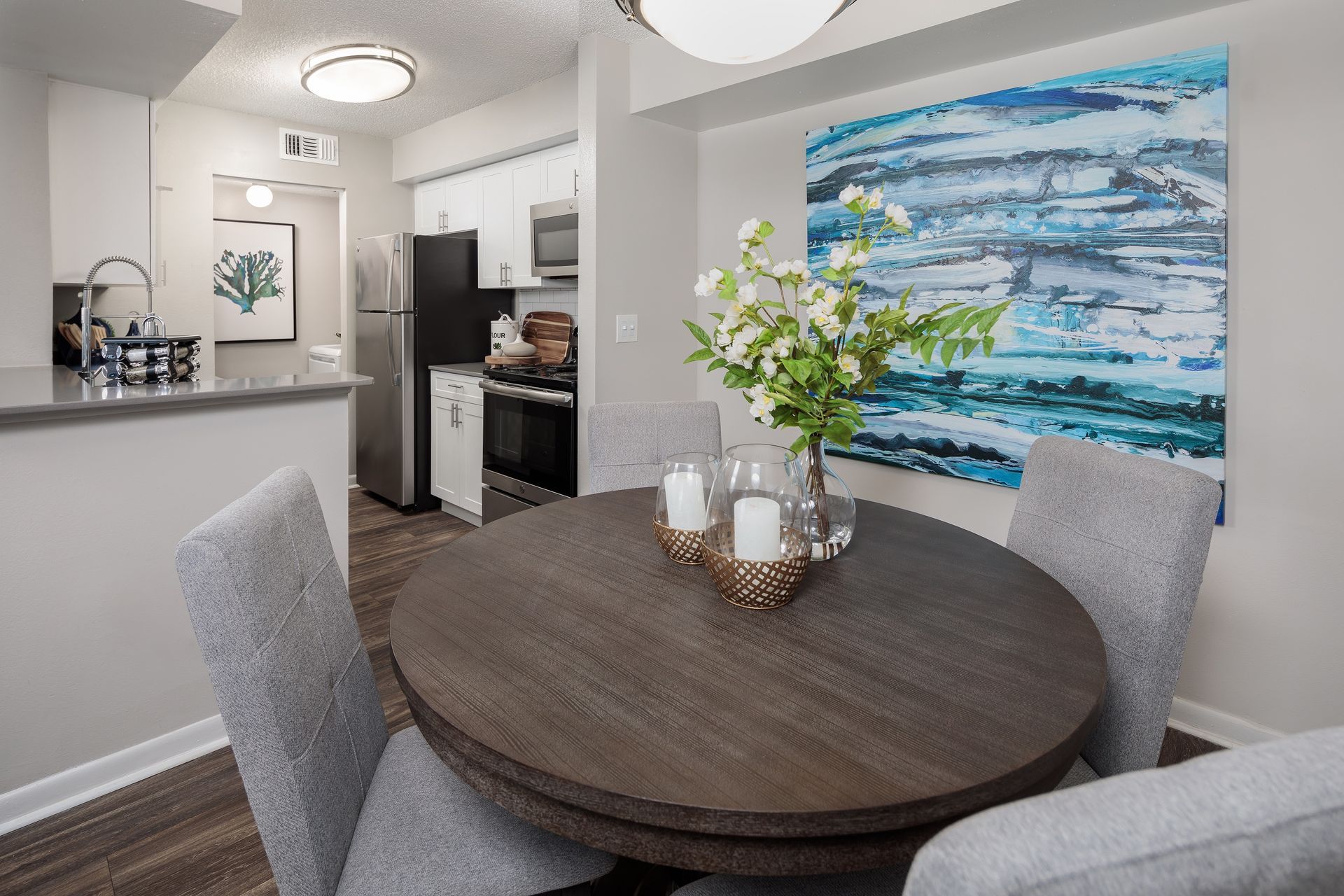 A dining room with a round table and chairs and a painting on the wall.