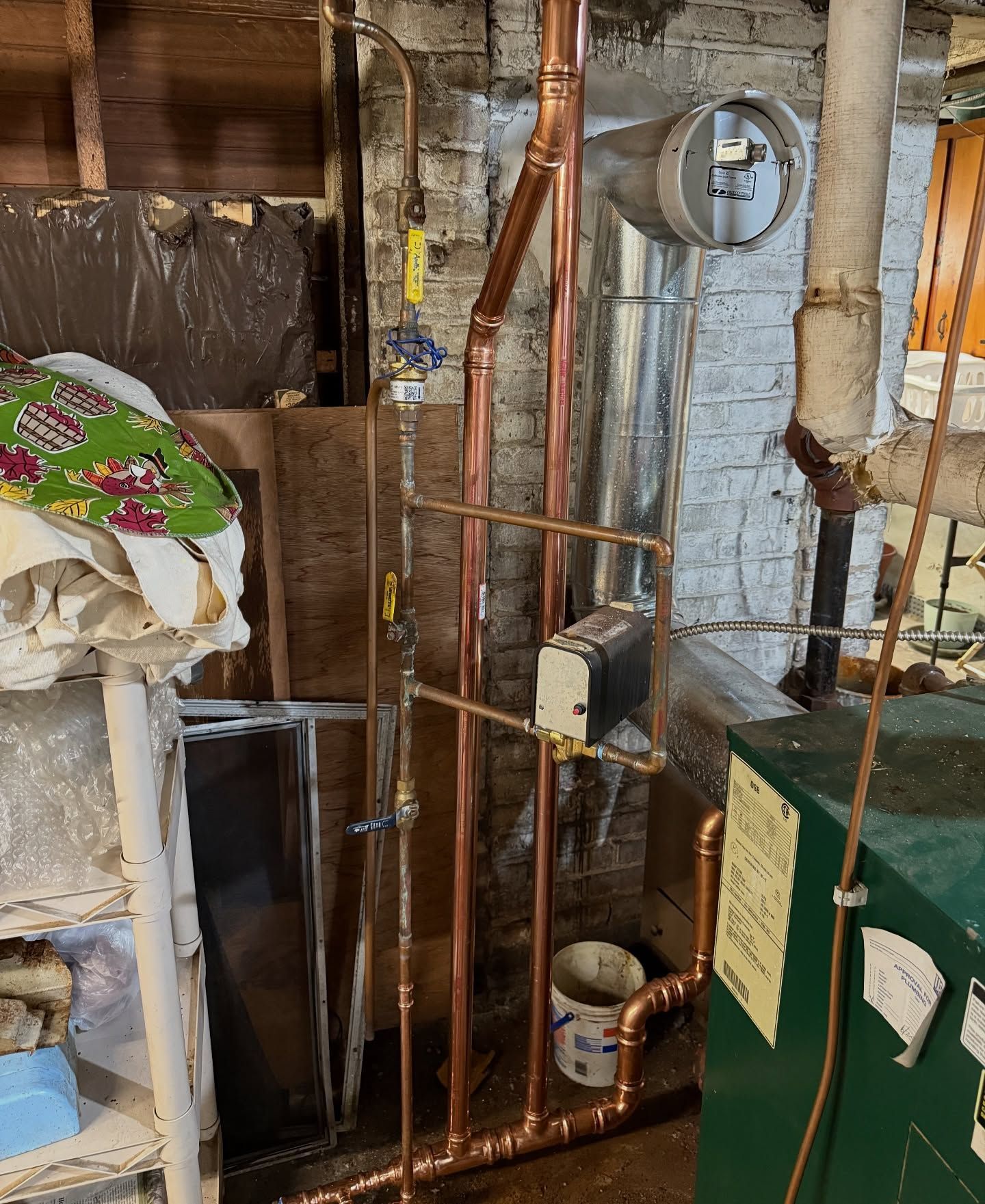 Copper pipes and valves against a brick wall in a basement, connected to a green water heater.