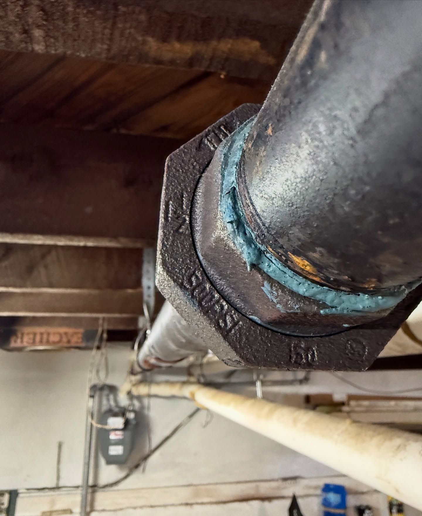 Black pipe with a bolted fitting, likely for gas lines, in a basement setting.