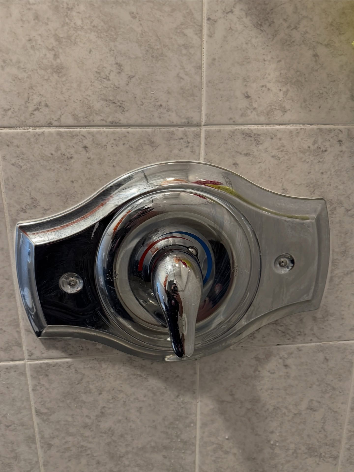 Chrome shower faucet with lever, mounted on gray tiled wall.