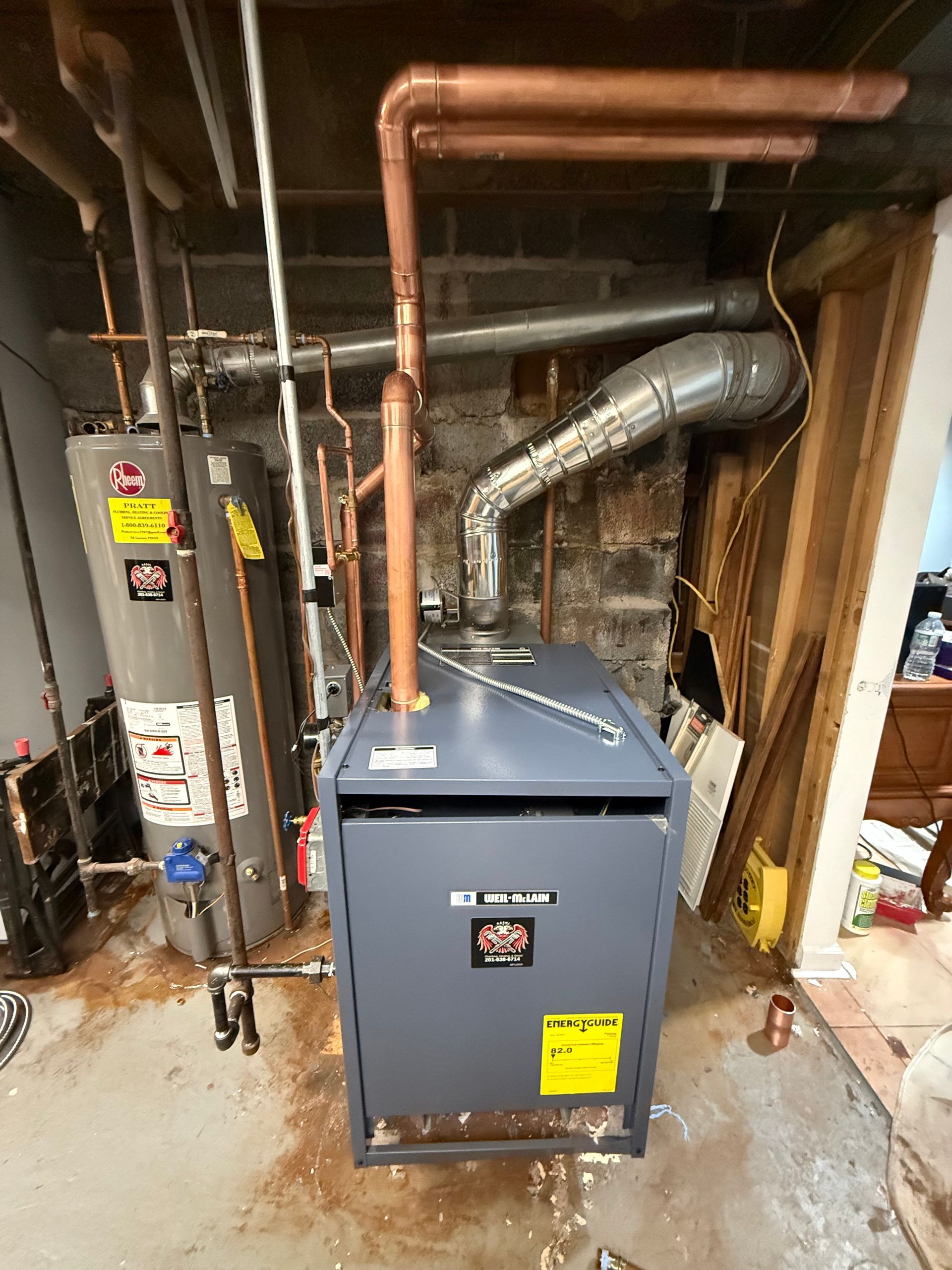 A newly installed gray furnace with copper pipes, a water heater, and ductwork in a basement.