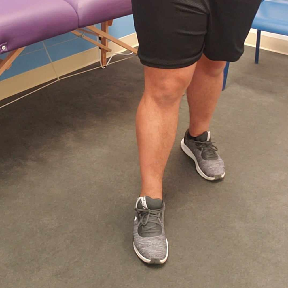 A person wearing black shorts and gray shoes is standing next to a purple bench