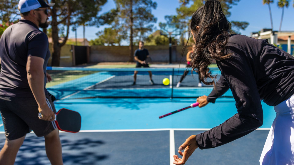 A man and a woman are playing pickleball on a tennis court.