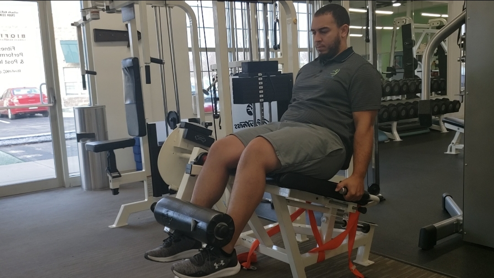 A man is sitting on a leg extension machine in a gym.