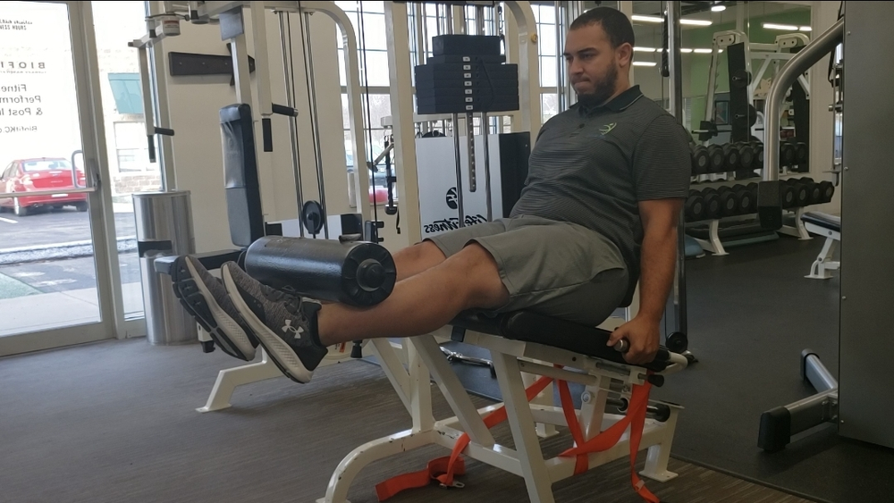 A man is sitting on a leg extension machine in a gym.