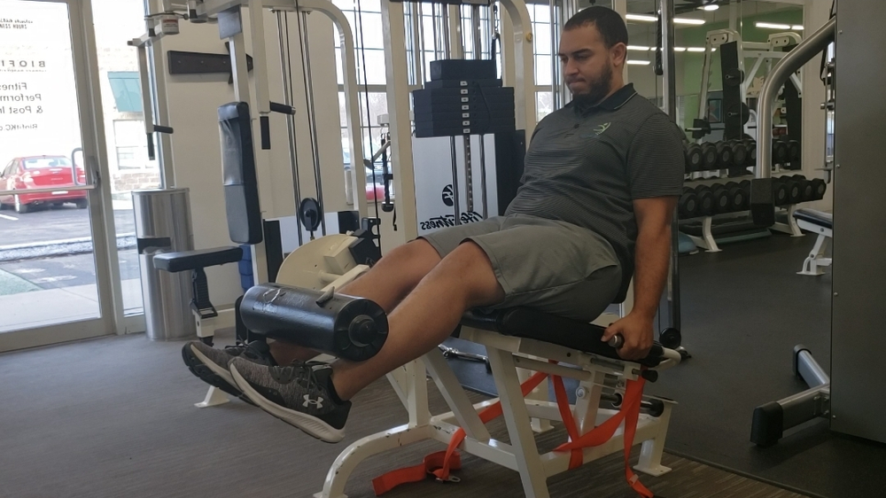 A man is sitting on a leg extension machine in a gym.