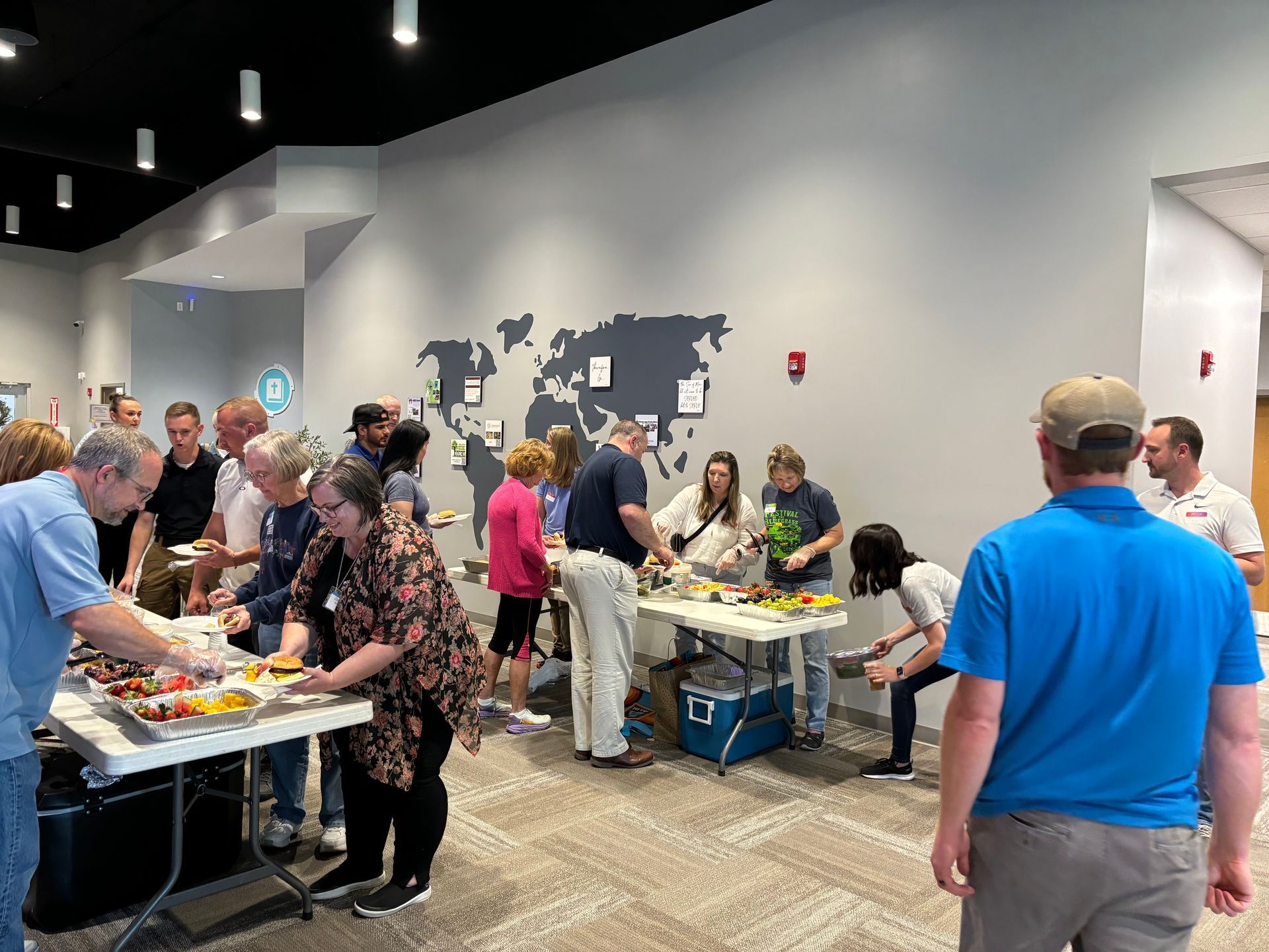 People at a buffet with food on tables against a wall with a map.