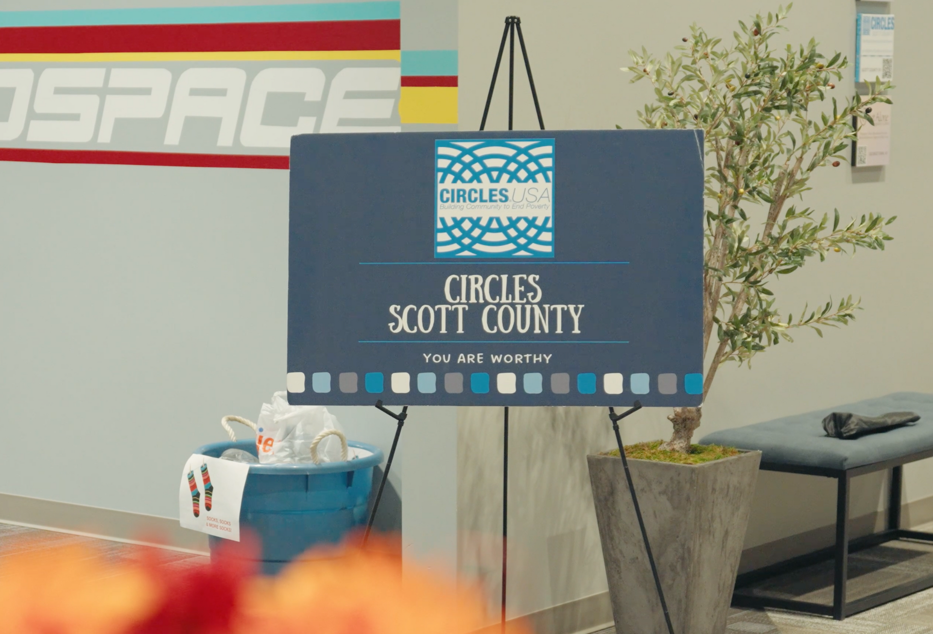 Sign for Circles Scott County on a blue easel, with an olive tree in the background.