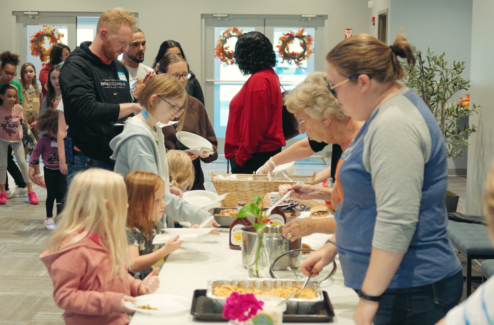People serving food at a buffet table; indoors with a crowd.