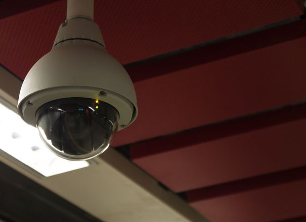 Security camera hanging from a red and white ceiling, monitoring the area.