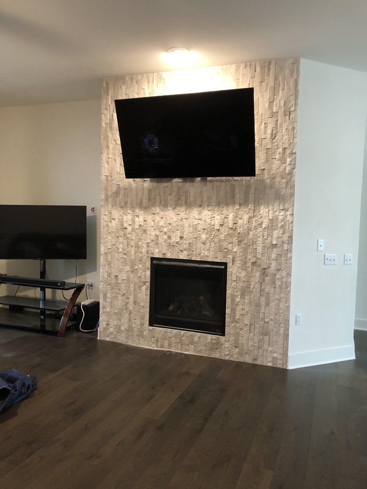 A living room with a fireplace, TV mounted above. Stone-like wall, dark floor and white wall.