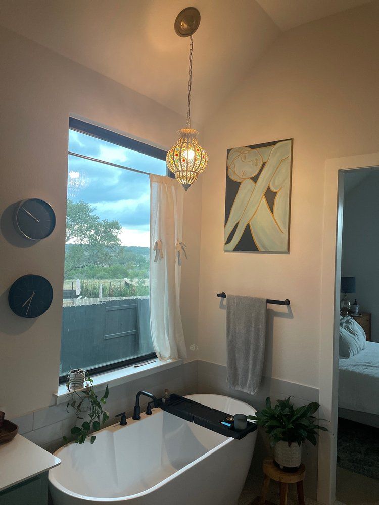 Bathroom with a white tub, window, art, and a hanging ornate light fixture.