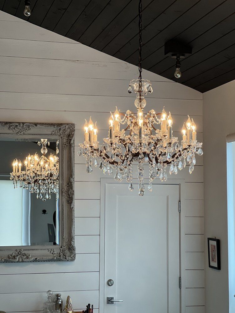 A large, ornate crystal chandelier hangs in a room with white paneled walls and a black ceiling.