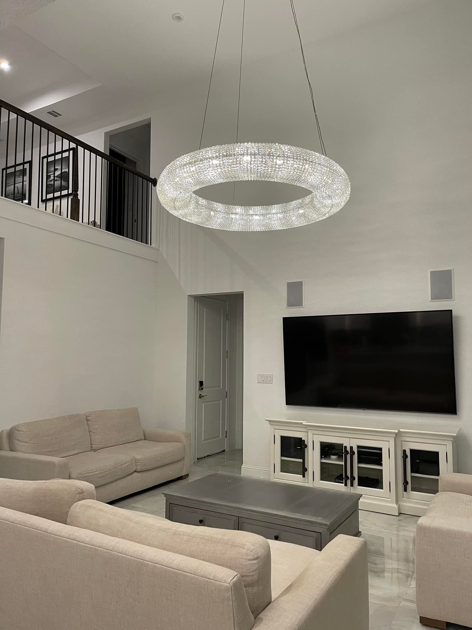 Living room with a large crystal chandelier, a TV, and beige couches.