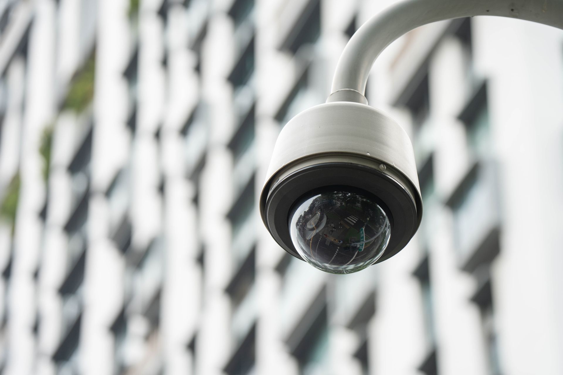 A security camera is hanging from a pole in front of a building.