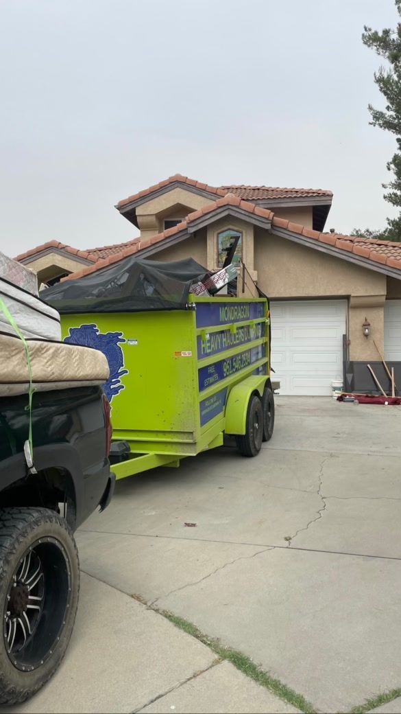 Green trailer, backed by a black truck, parked in front of a house on a cloudy day.