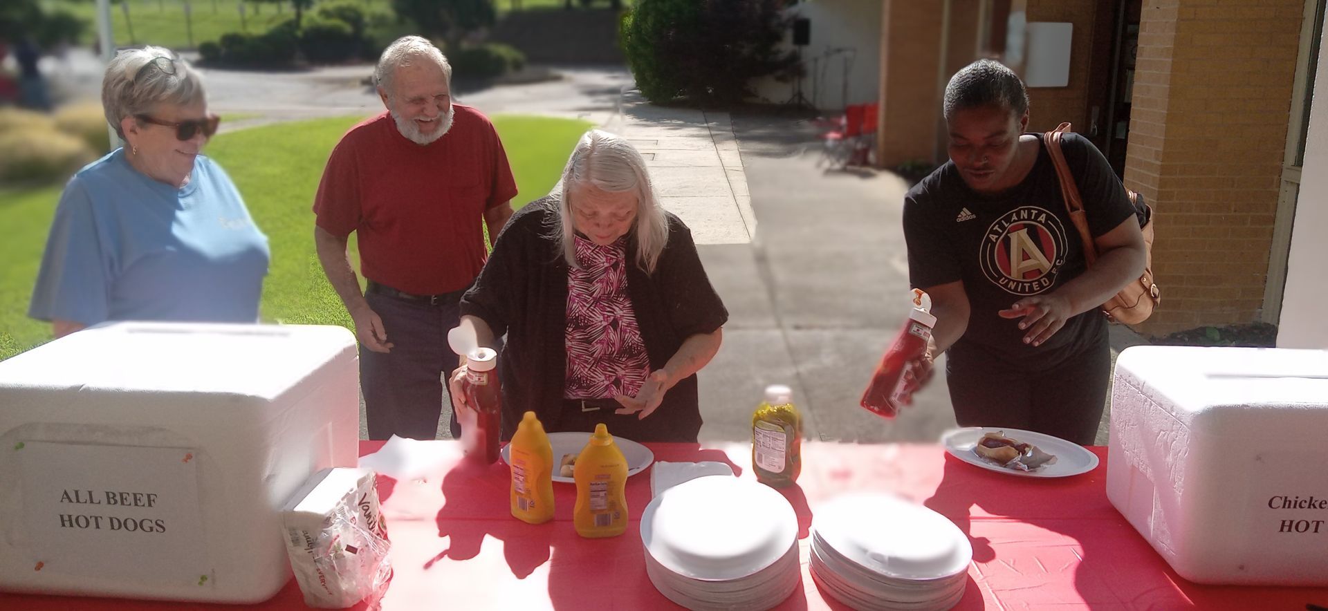A group of people are standing around a table with plates and condiments on it.