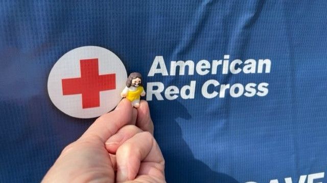A person is holding a toy in front of an american red cross sign