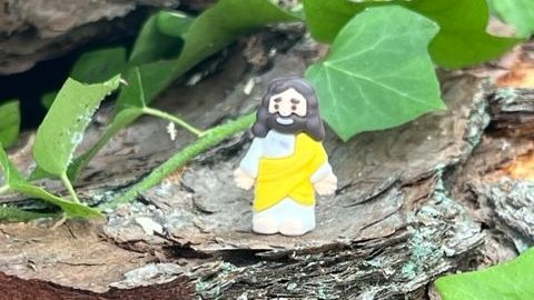 A small figurine of jesus is sitting on a piece of wood.