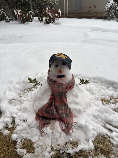 A snowman wearing a hat and scarf is sitting in the snow.