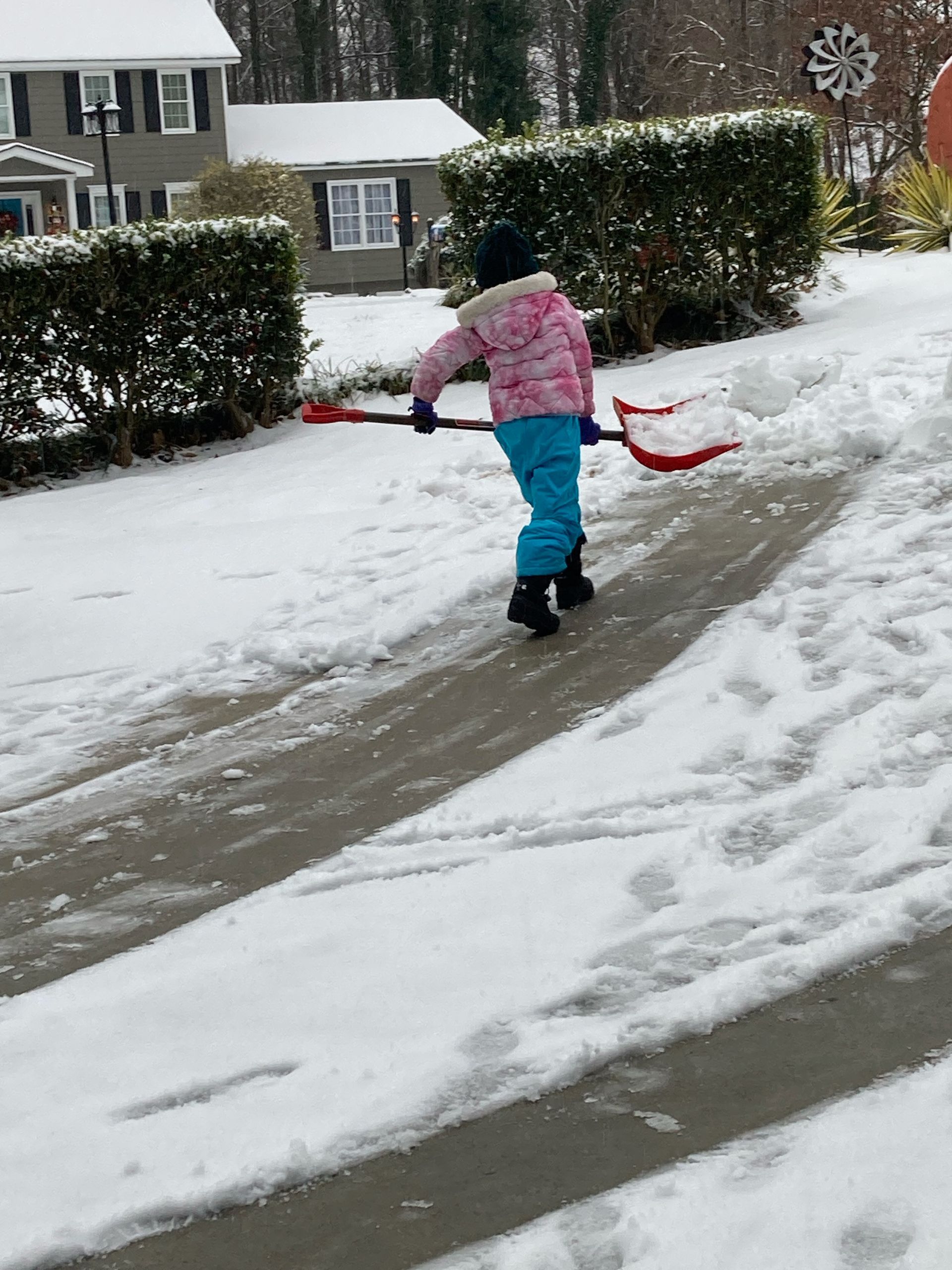 A little girl in a pink jacket is shoveling snow