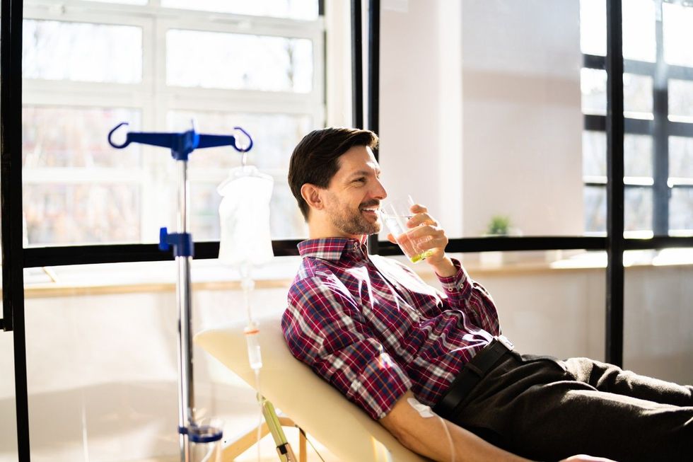 a man is laying in a hospital bed drinking a glass of water