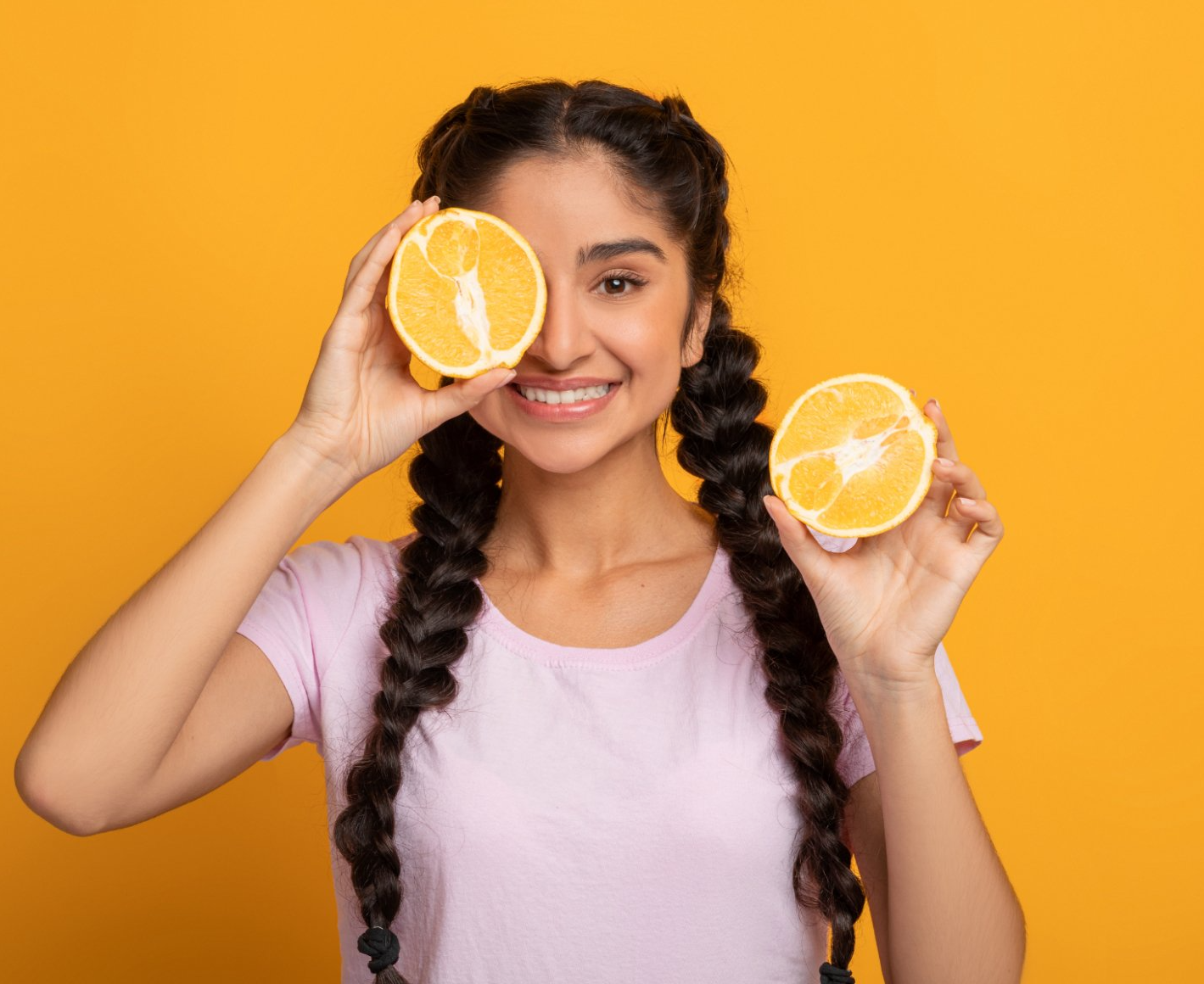 teen girl holding cut orange over eye