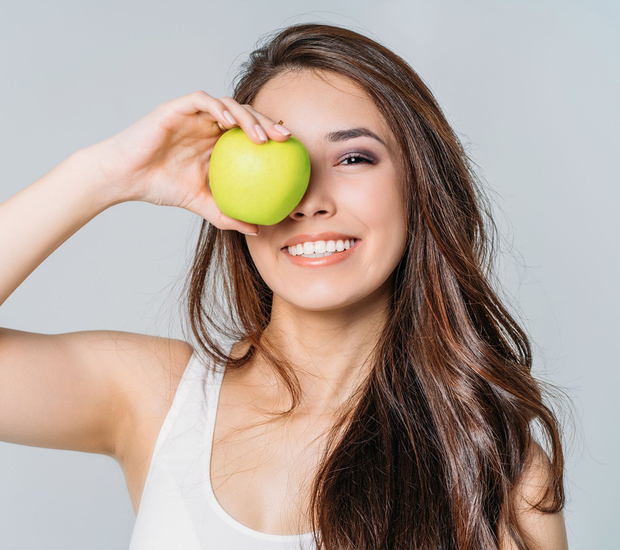 young woman holding green apple over eye