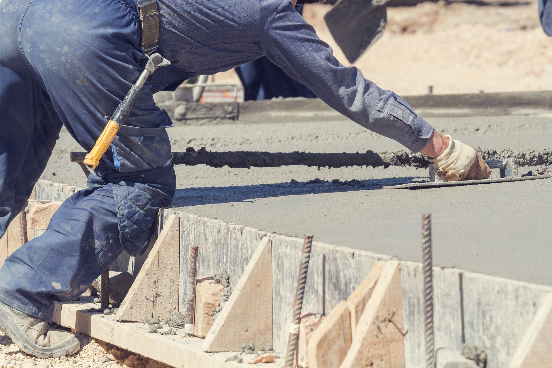Construction worker smoothing wet concrete on a form with a hand trowel.