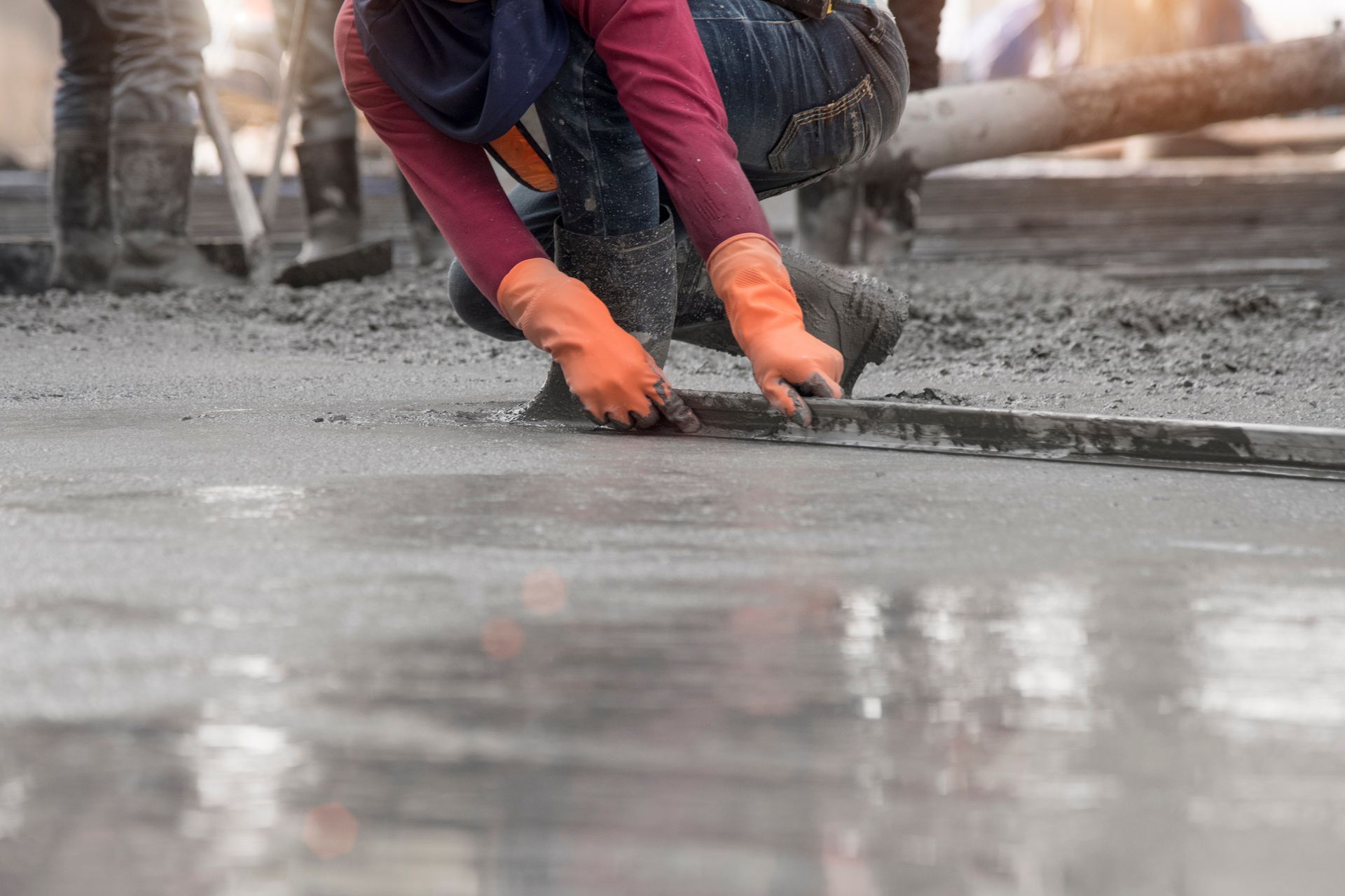 Worker in orange gloves smoothing freshly poured wet concrete with a hand trowel