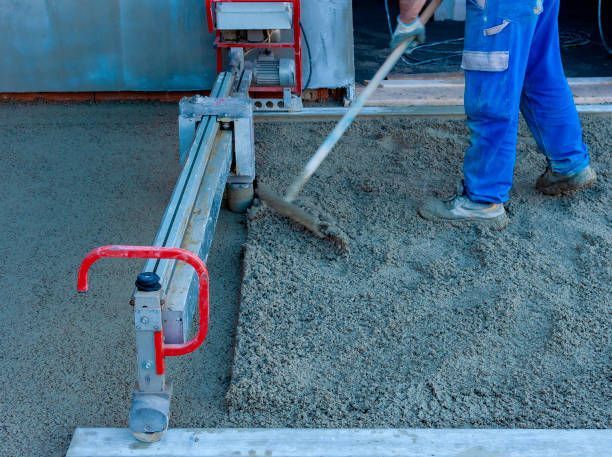 Worker leveling fresh concrete with screed machine for smooth industrial floor finish.