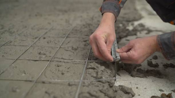 Hands installing metal rebar mesh in wet concrete for reinforced flooring construction.