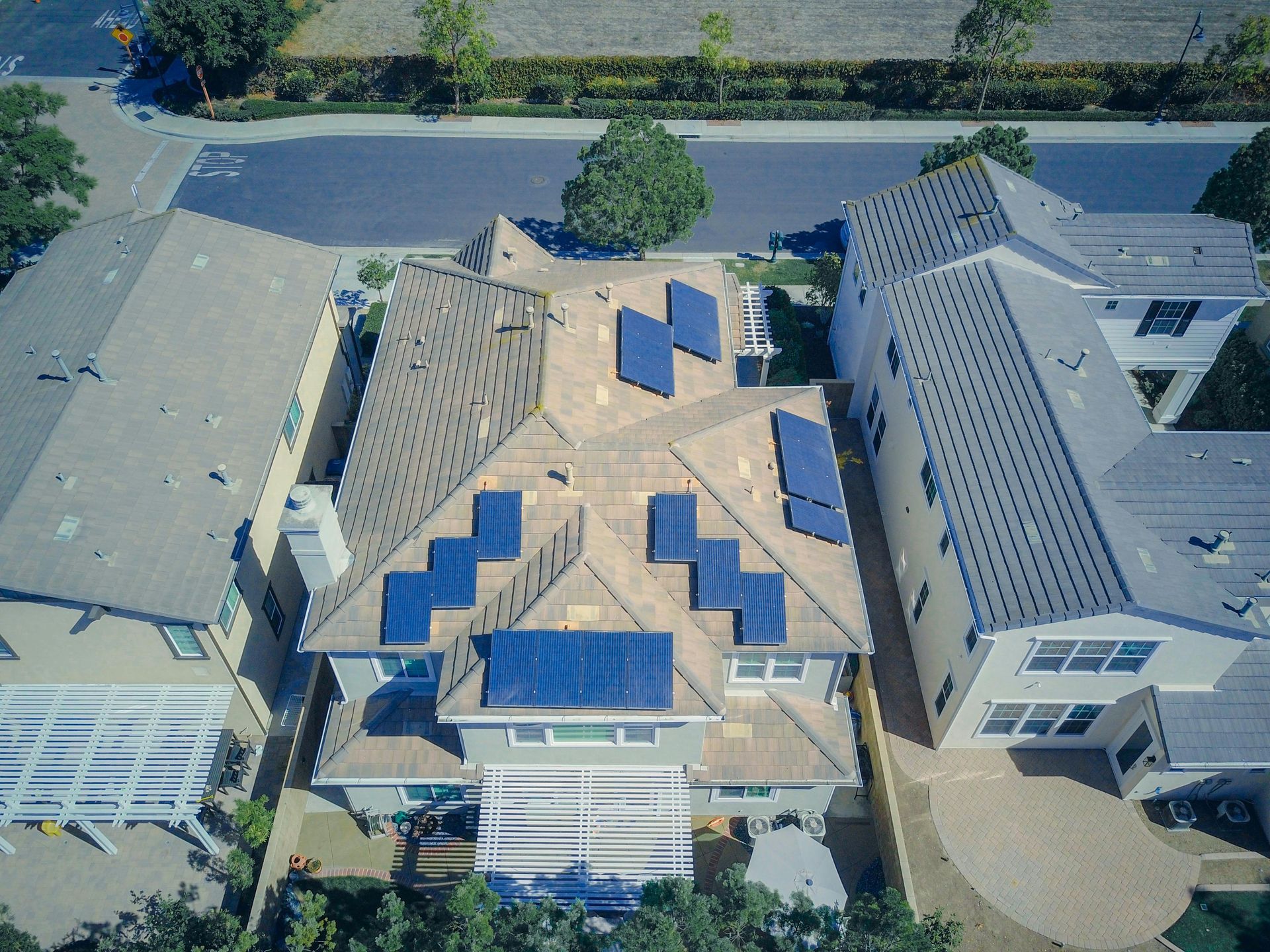 Aerial view of a house with solar panels on the roof, surrounded by other houses and a street.