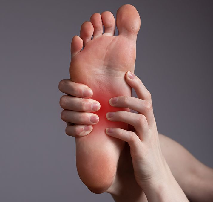 Hands massaging the sole of a foot with a red, irritated arch on a gray background