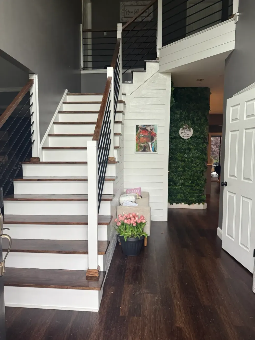 Interior entry hall with white staircase, dark wood floors, and a potted flower arrangement.