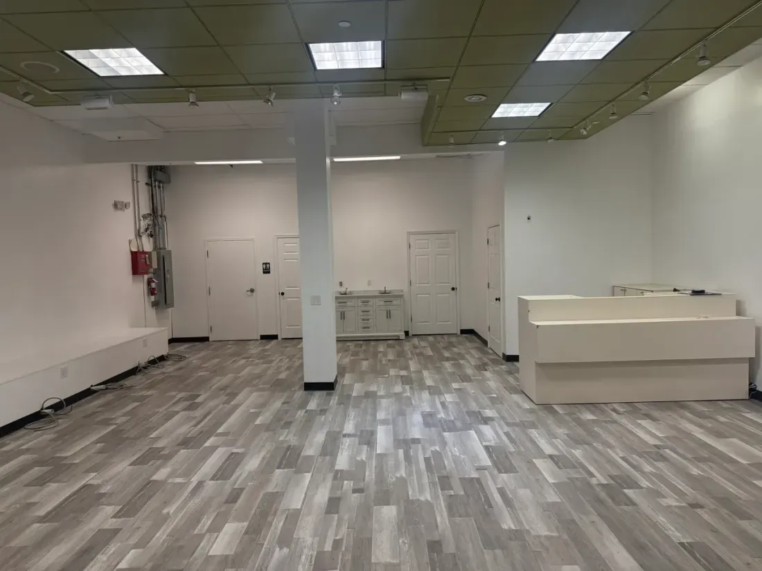 Empty retail interior with gray flooring, white walls, fluorescent ceiling lights, and a counter on the right