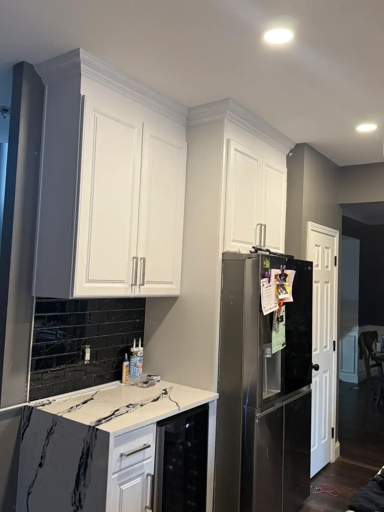 Modern kitchen with white cabinets, black appliances, and dark gray walls, viewed along the counter.