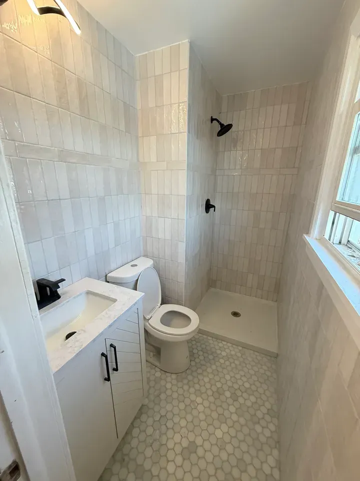 Small tiled bathroom with vanity, toilet, and walk-in shower in beige tones.