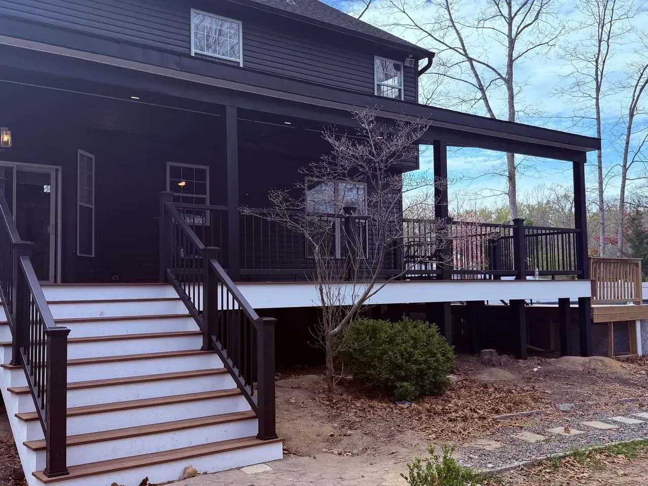 Front porch of a dark house with white stairs, black railings, and a wooden deck under a roofed overhang.