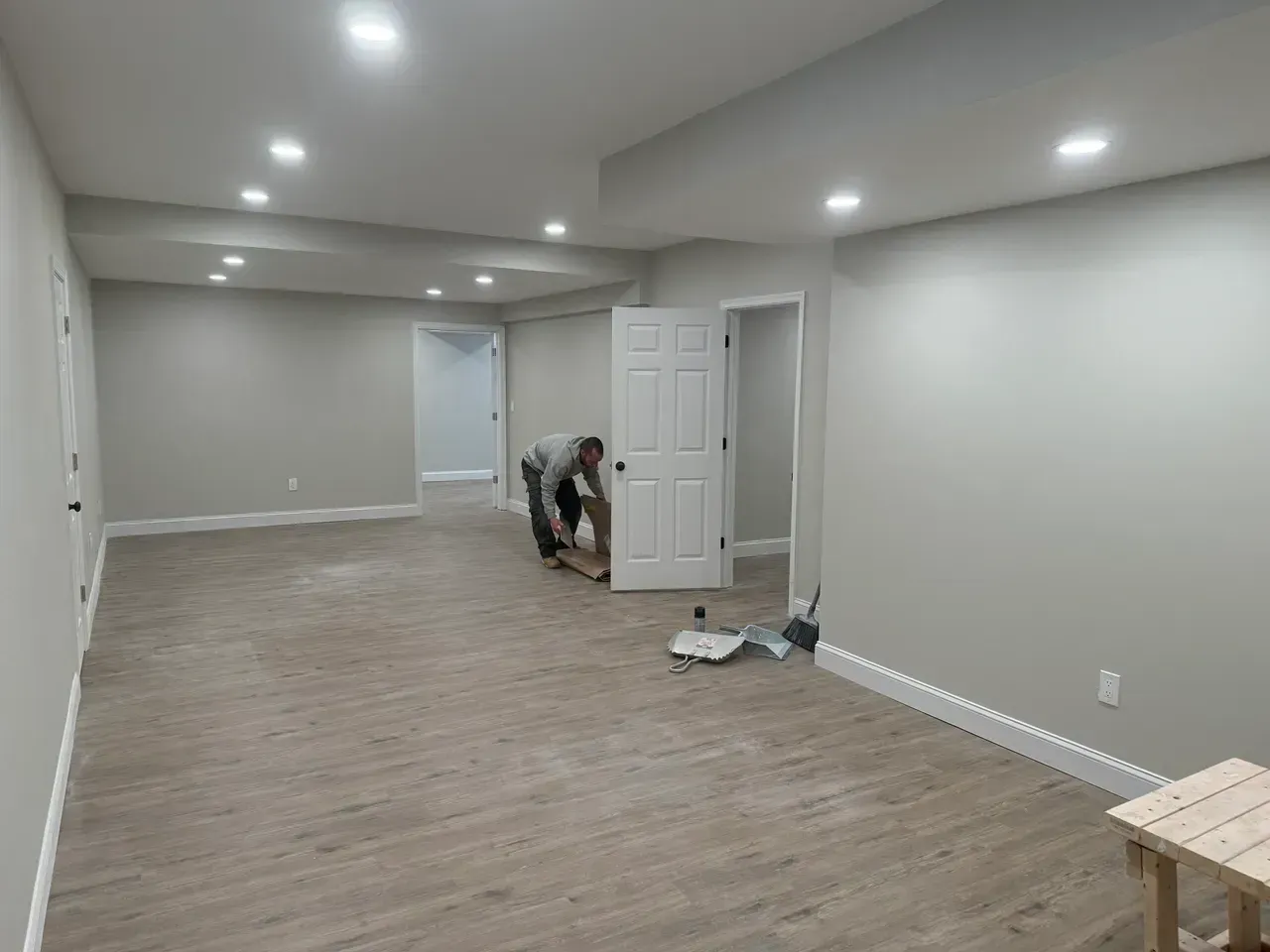 Empty gray room with wood floors; worker near open doors and tools on the floor.
