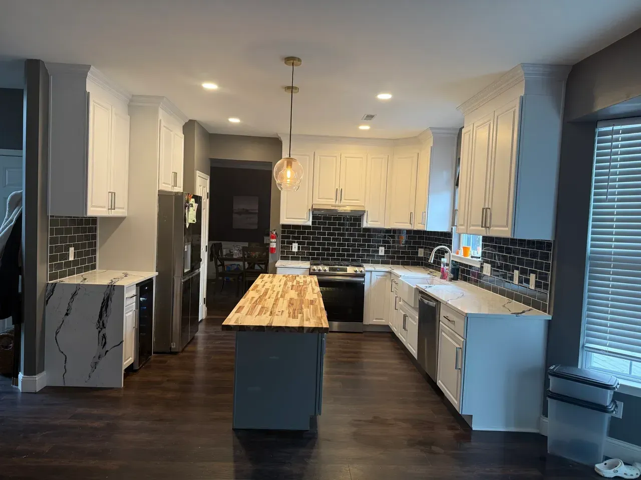 Modern kitchen with white cabinets, dark backsplash, and a wooden island under pendant lights.