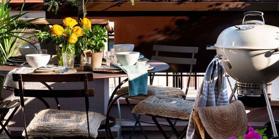Una mesa y sillas en un balcón con una parrilla al fondo.