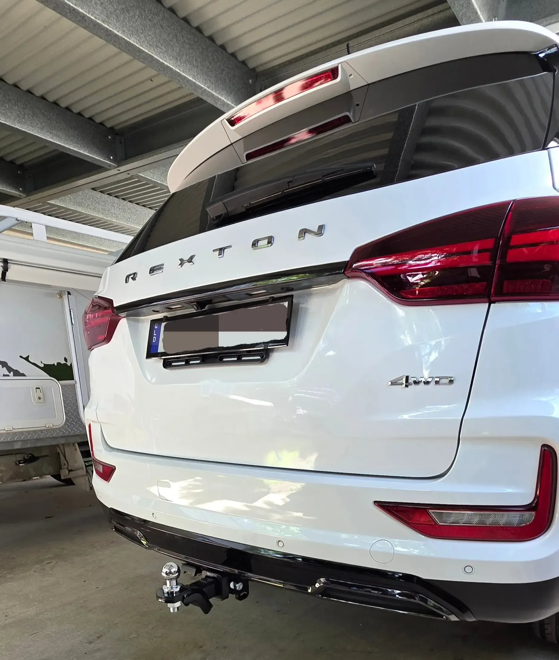 White SsangYong Rexton SUV with a tow hitch, parked under a shelter. Rear view with 4x4 emblem. — Hinterland Towbar & Steel Fabrication In Cooroy, QLD